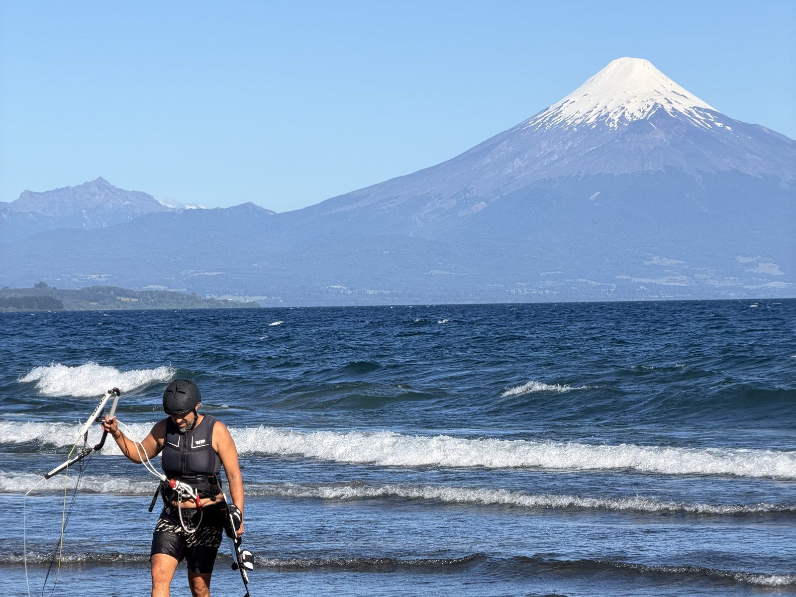 Kitesurfista revisando la barra con el agua por las rodillas, con el volcán Osorno al fondo
