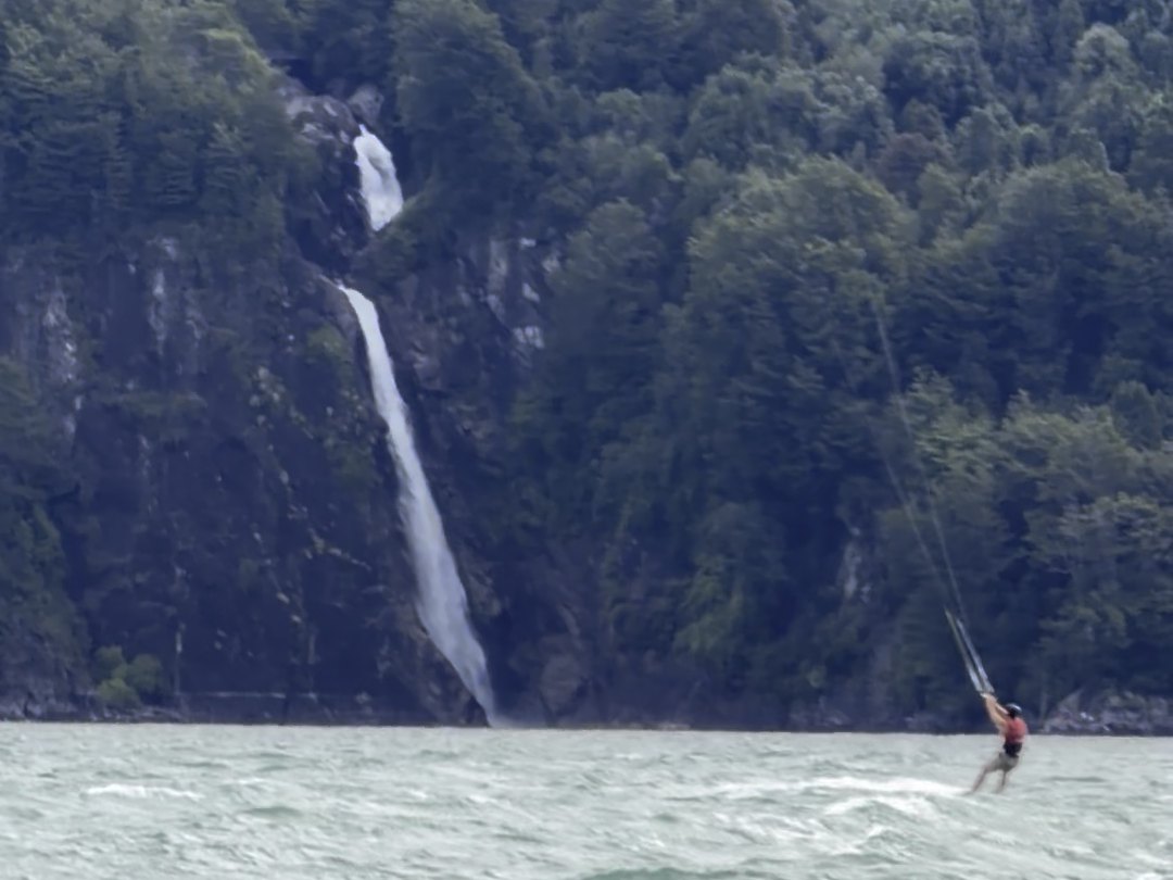 Kitesurfista navegando frente a la cascada que baja por la ladera del lago Tagua Tagua