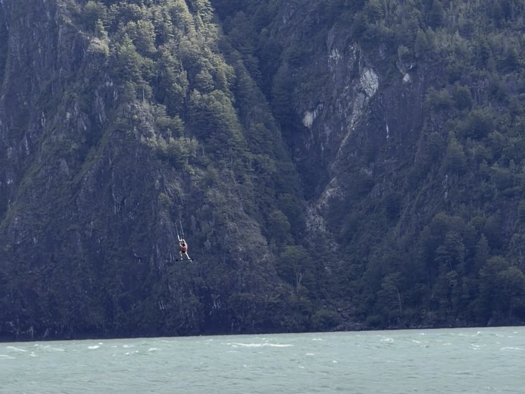 Una cometa diminuta contra la pared de bosque que encajona el lago